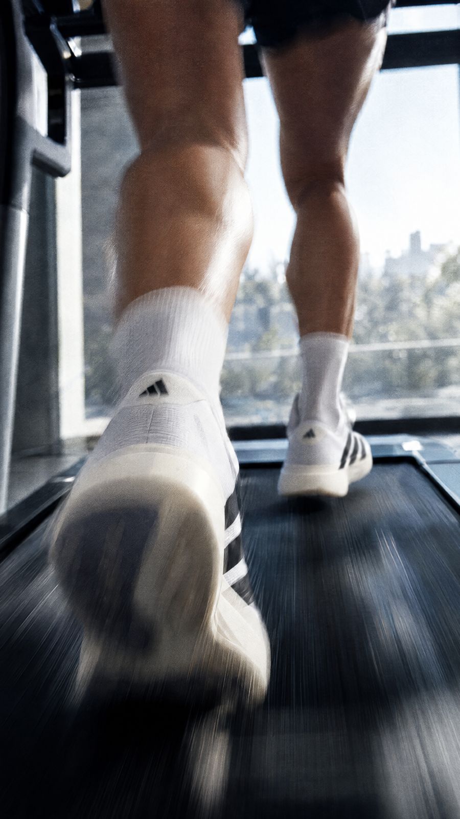 White running shoes blurred mid-stride on a treadmill belt, a bright window behind.