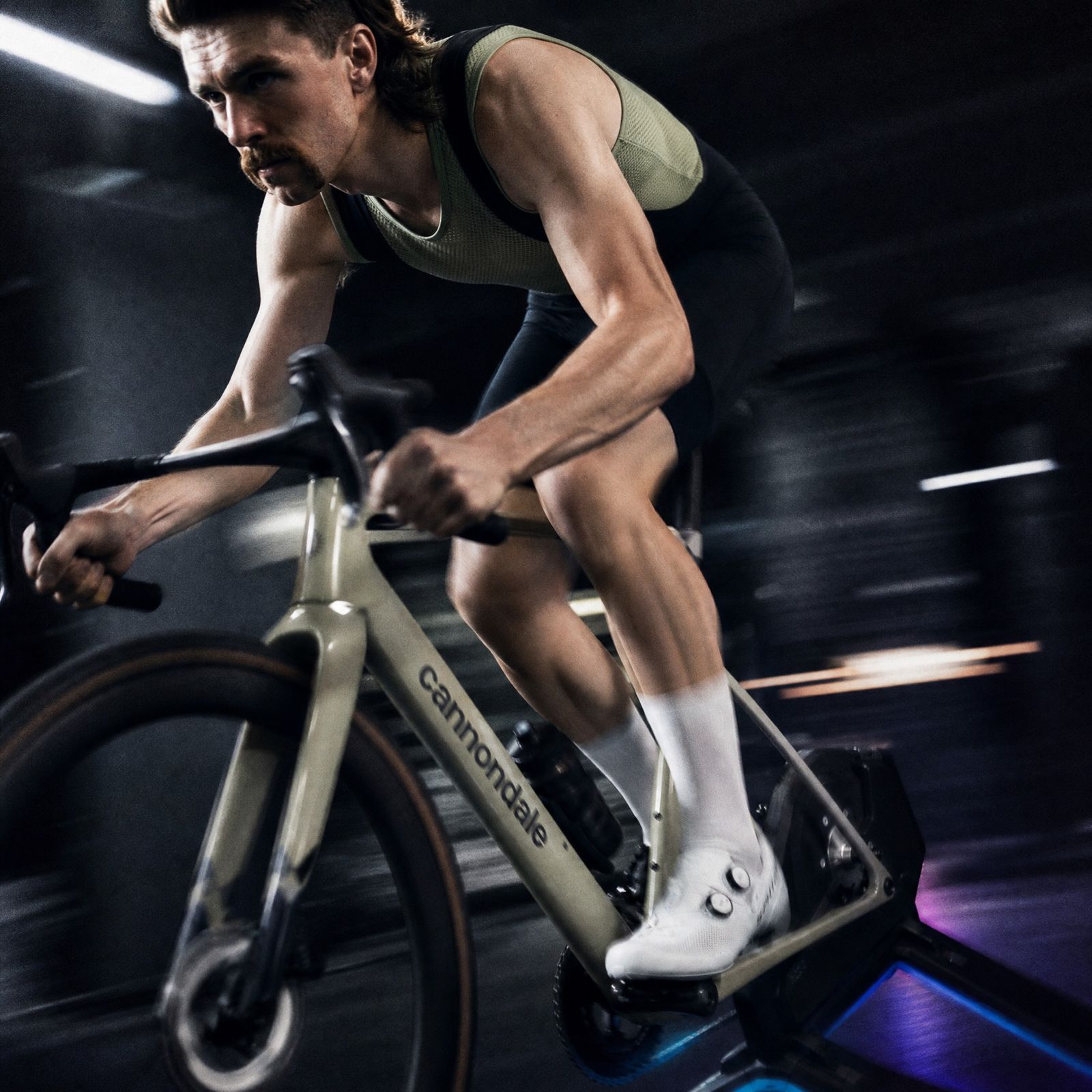 A rider low over the bars on a trainer, the dark room streaking past in the blur.